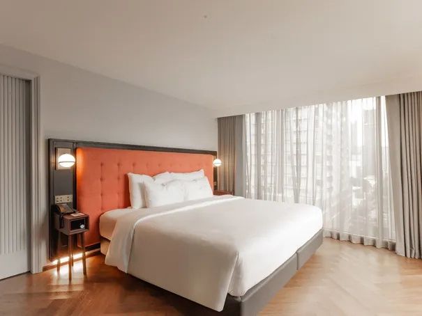 Großes Doppelbett mit orangefarbenem Kopfteil und Vorhängen vor der Fensterfront.