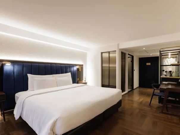 Hell eingerichtetes Hotelzimmer mit einem Doppelbett und Blick zum Badezimmerbereich.