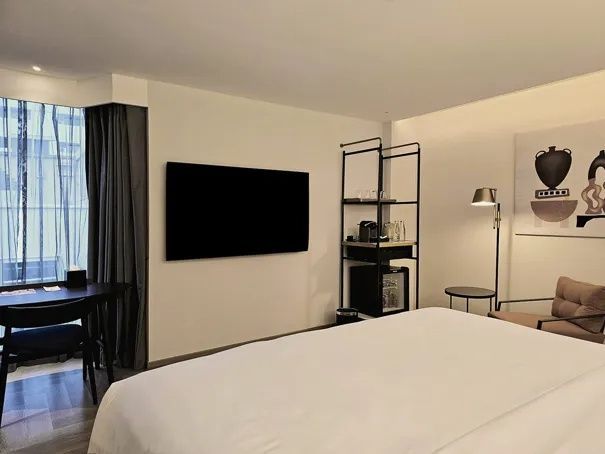 Hotelzimmer mit Blick auf flachen Fernseher und offenes schwarzes Regalsystem.