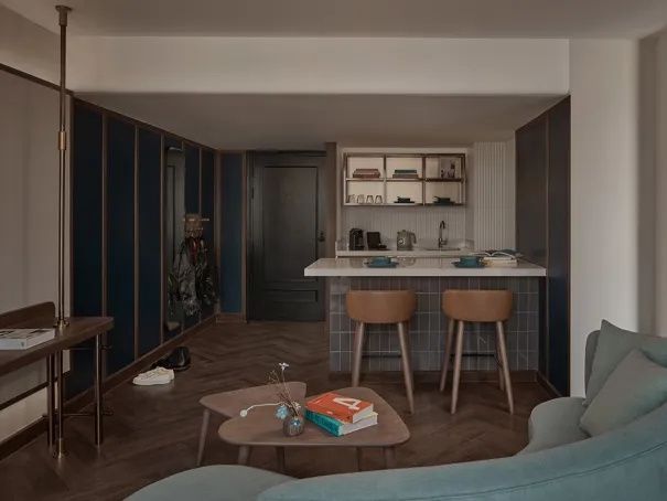 Wohnraum mit Parkettboden, Couchtisch, blauer Wand und hinterer Küchenzeile.