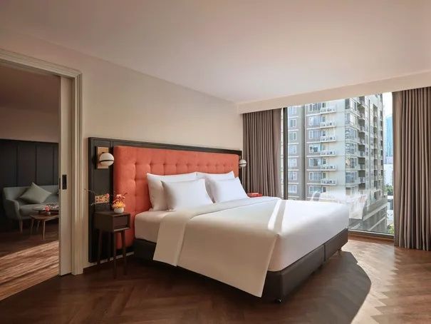 Doppelbett mit gepolstertem Kopfteil in Orange und bodentiefem Fenster im Zimmer.