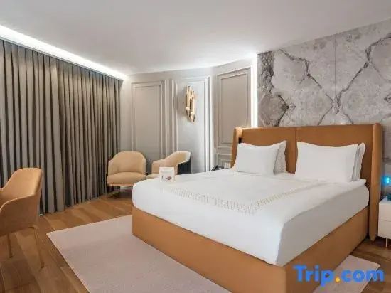 Modernes Hotelzimmer mit hellbraun gepolstertem Doppelbett, Marmorwand und Sesseln.