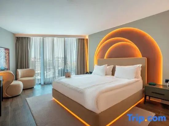 Großes Hotelzimmer mit beleuchtetem Bettkopfteil, Vorhängen und bodentiefen Fenstern.