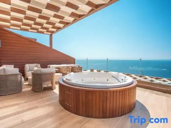 Holzterrasse mit rundem Whirlpool und Sitzbereich mit freiem Blick auf das blaue Meer.