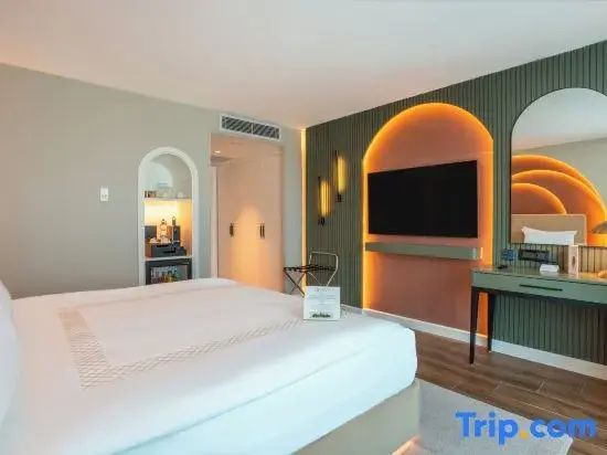 Blick im Hotelzimmer auf das Bett und eine beleuchtete Wand mit Fernseher und Schreibtisch.