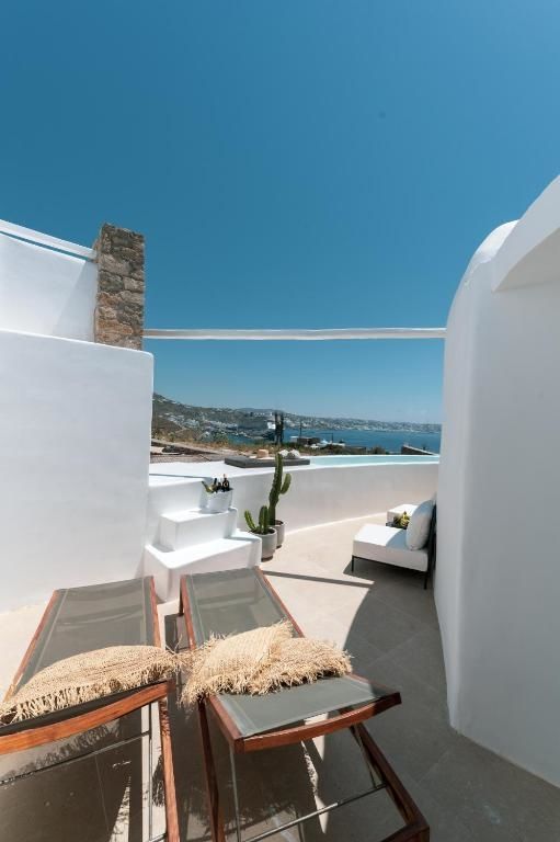 Weiße Hotelterrasse mit Sonnenliegen und Blick auf das Meer und die Küste von Mykonos.