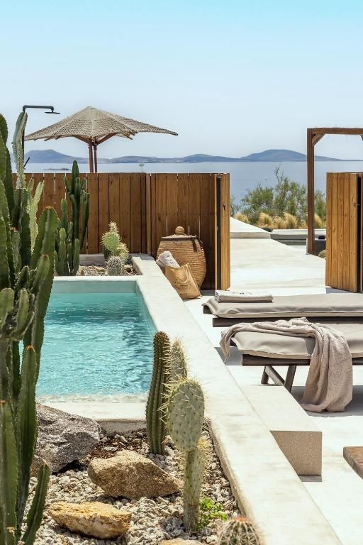 Pool mit türkisblauem Wasser neben Kakteen und Sonnenliegen mit Meerblick.