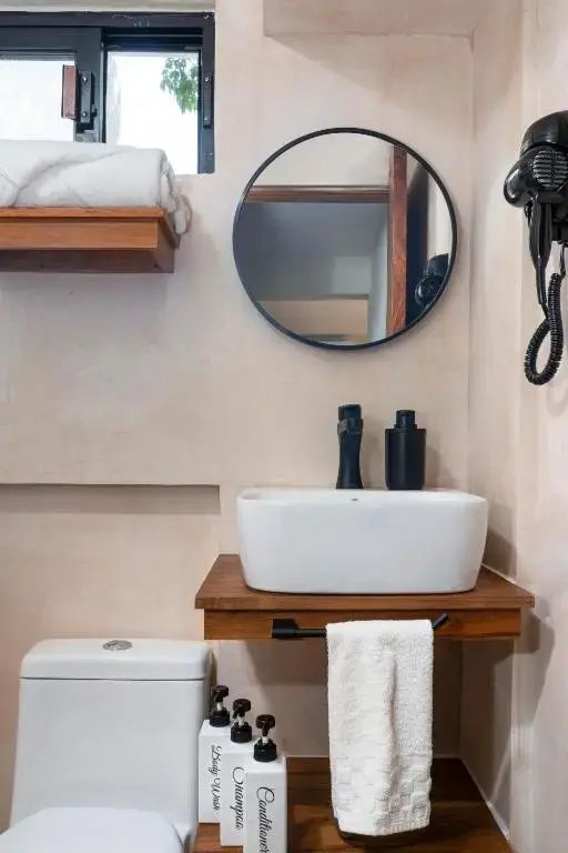 Badezimmer mit weißem Aufsatzwaschbecken auf Holzkonsole, rundem Spiegel und Handtüchern.