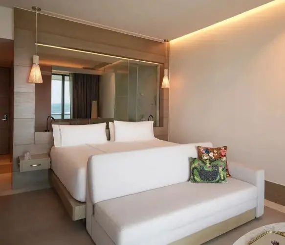 Helles Hotelzimmer mit großem Doppelbett, weißem Sofa und modernem Spiegel.