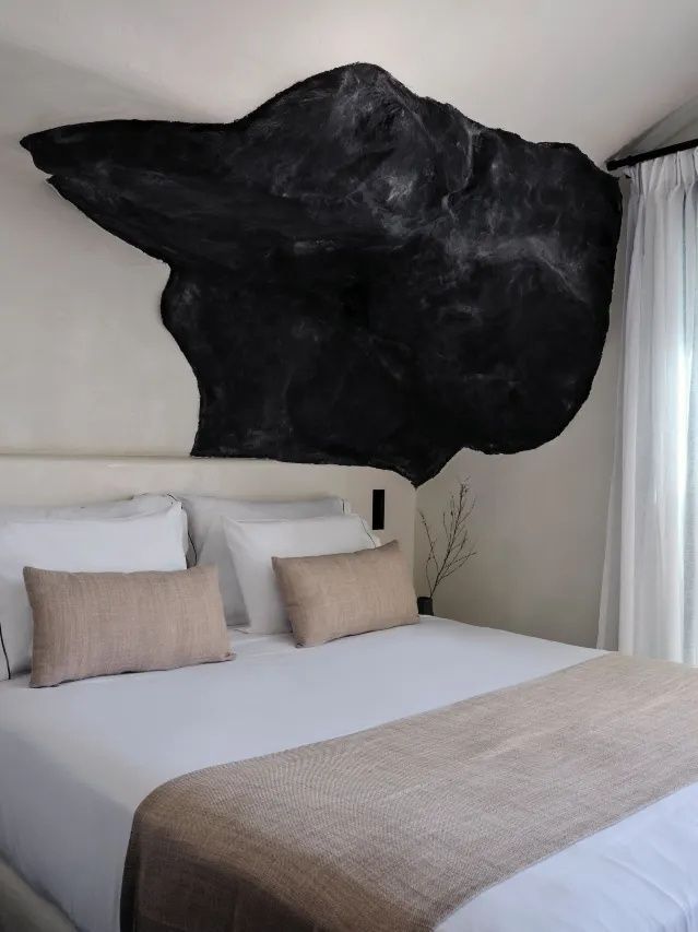 Doppelbett mit weißen Kissen und einer dunklen Felsinstallation an der Wand.