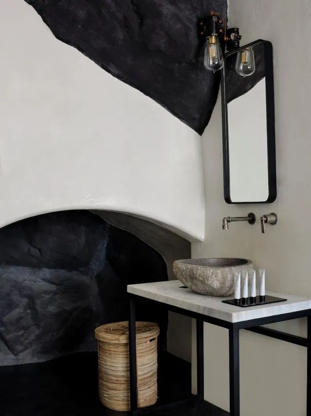 Waschtisch mit Steinschale, schwarzem Spiegel und dunklen Akzenten an der Wand.
