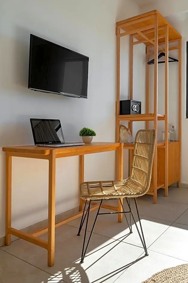 Schreibtisch aus Holz mit Stuhl aus Geflecht, Laptop und Fernseher an der Wand.