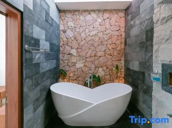 Freistehende weiße Badewanne in einem Badezimmer mit dunklen Steinwänden.