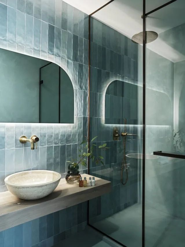 Badezimmer mit blauen Wandfliesen, einem runden Aufsatzwaschbecken und beleuchtetem Wandspiegel.