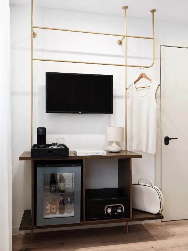 Offene Garderobe aus Metall mit Fernseher, Minibar, Zimmersafe und einer kleinen Tischlampe.