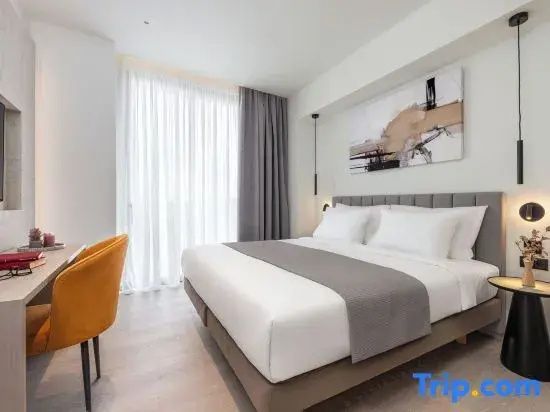 Helles Hotelzimmer mit großem Doppelbett, Vorhängen und einem gelben Stuhl am Fensterrand.