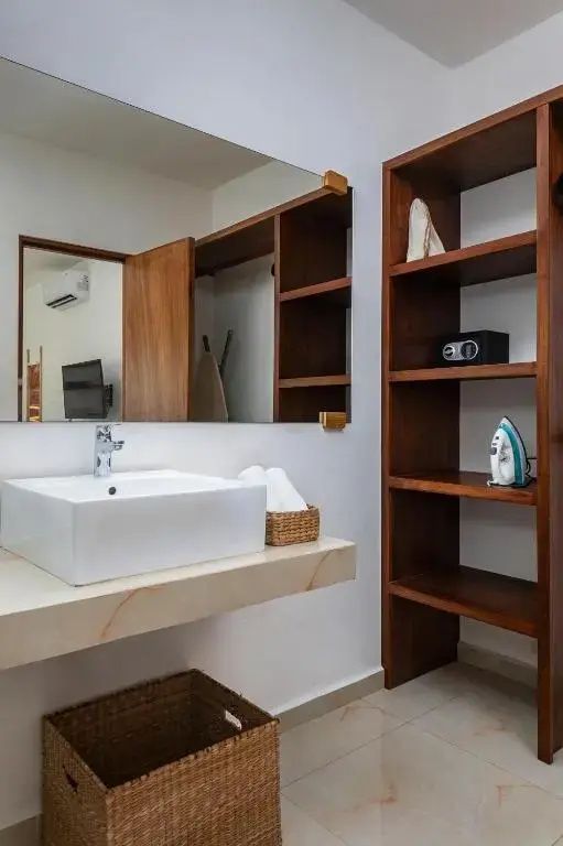 Modernes Waschbecken mit großem Spiegel und ein hohes Holzregal mit Bügeleisen.