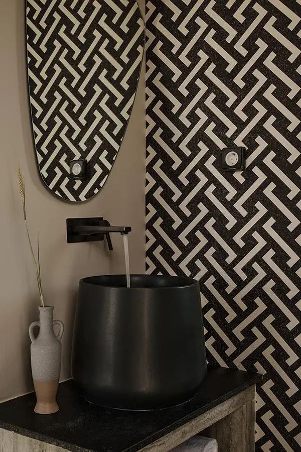 Schwarzes Waschbecken mit laufendem Wasserhahn vor schwarz weißer Musterwand.