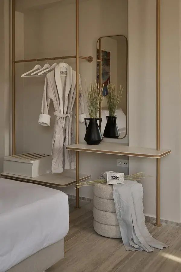 Offener Kleiderständer aus Metall mit Bademantel, Kleiderbügeln, Deko und kleiner Sitzgelegenheit.