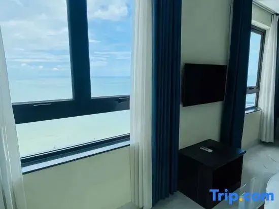 Blick aus dem Zimmerfenster auf das blaue Meer unter leicht bewölktem Himmel.