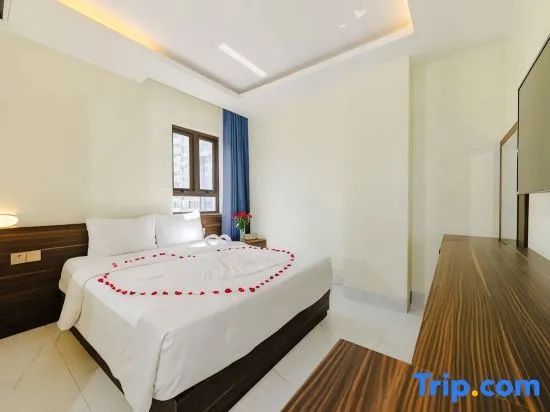 Helles Hotelzimmer mit Doppelbett, Fensterecke und dekorativer Herzform aus Blüten.