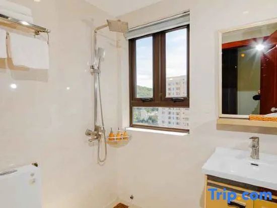 Badezimmer mit Dusche, Fenster, Wandspiegel und einem Waschbecken mit Unterschrank.