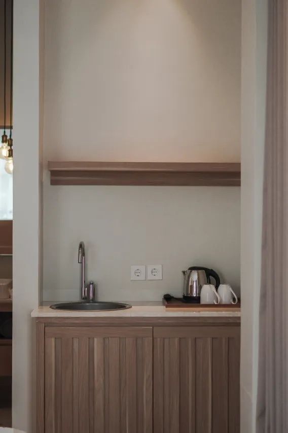 Kleine Küchenzeile im Zimmer mit Spülbecken, Wasserkocher, zwei Tassen und Holzschrank.