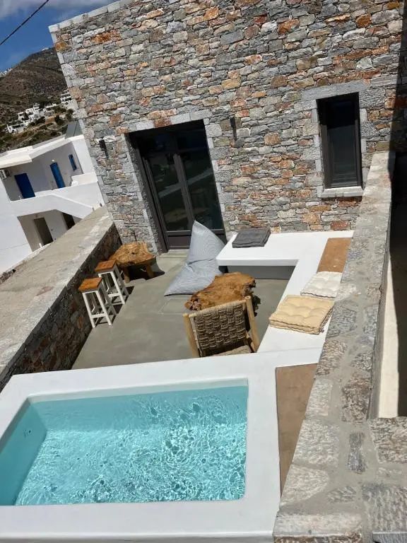 Terrasse mit kleinem Pool, Holzhockern, Sitzkissen und Natursteinmauer.