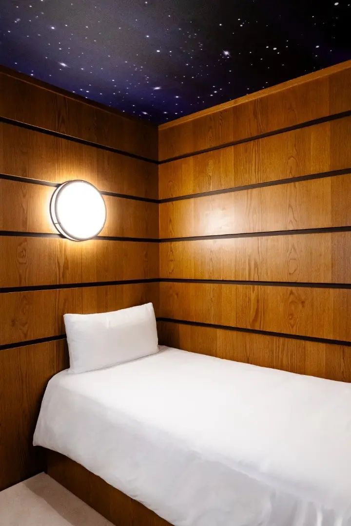 Kleine Schlafnische mit Holzverkleidung, Einzelbett und runder Wandleuchte.