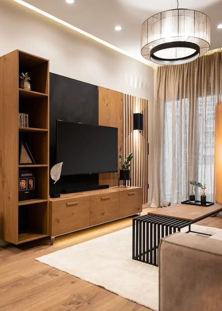 Wohnbereich mit einem Flachbildfernseher auf einer Holzschrankwand, Couch und Vorhängen.