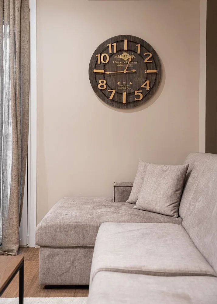 Sitzbereich mit einer hellen Eckcouch und einer großen Wanduhr an der beigen Wand.