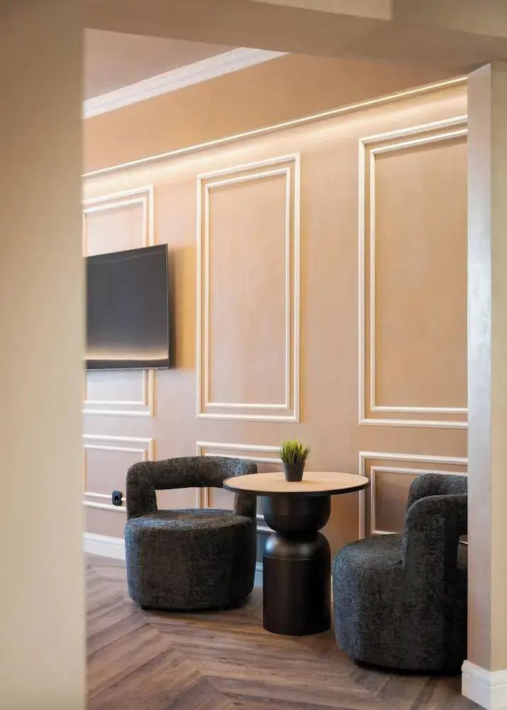 Sitzbereich in der Suite mit zwei dunklen Sesseln, einem kleinen Tisch und Wand-TV.