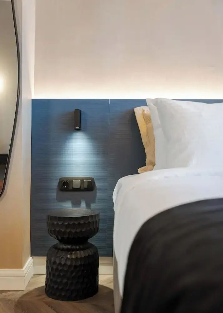 Bett mit weißem Kissen, blau gestalteter Kopfteil-Wand, Wandleuchte und Beistelltisch.