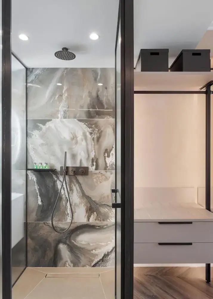 Badezimmer mit moderner Dusche aus Marmorfliesen und angrenzendem Garderobenschrank.