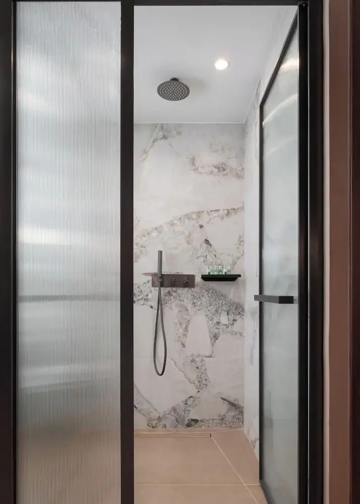 Moderne Dusche mit marmorierten Fliesen, Regenduschkopf und Glaselementen.
