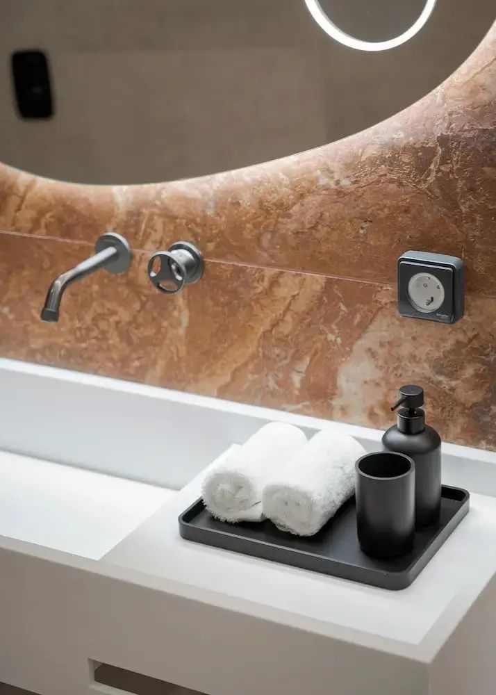Waschtischbereich im Badezimmer mit Marmorwand, dunkler Armatur und Zubehör auf einem Tablett.