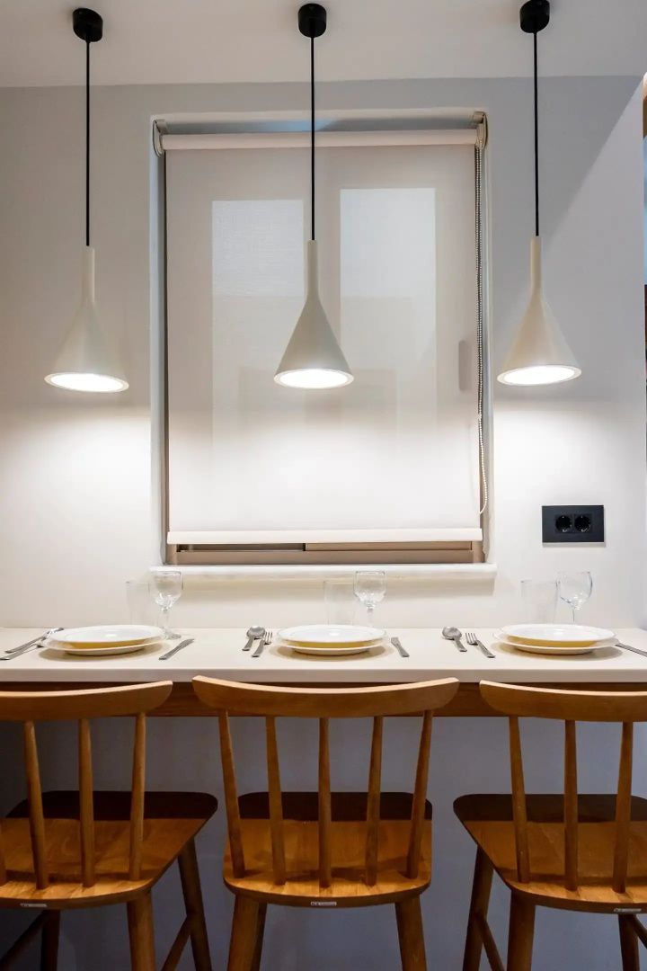 Gedeckter Esstisch mit drei Holzstühlen und hängenden Lampen an einer hellen Wand.