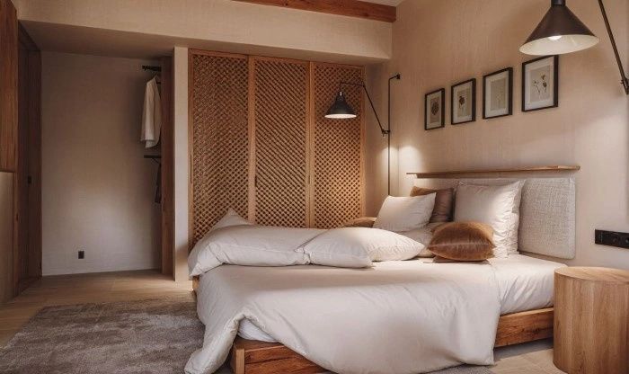 Doppelbett mit hellen Kissen und Holzrahmen vor einem Einbauschrank mit Geflechtfronten.