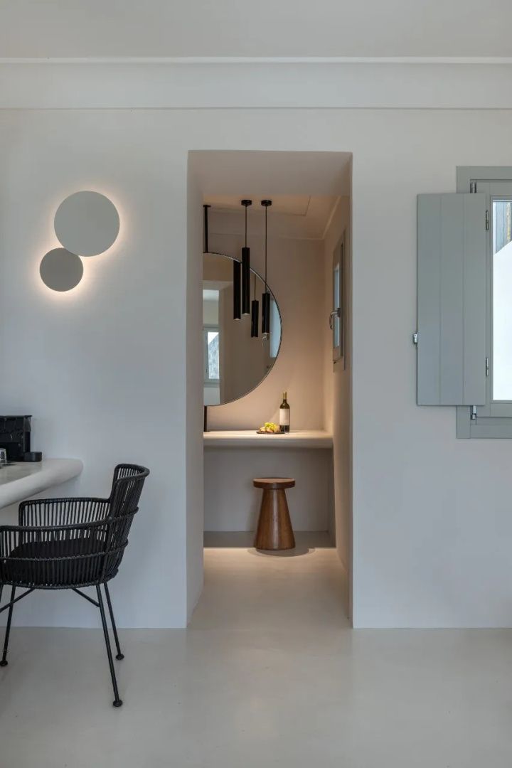 Minimalistisch gestalteter Innenraum mit beleuchtetem Spiegel, modernem Stuhl und Holzhocker.