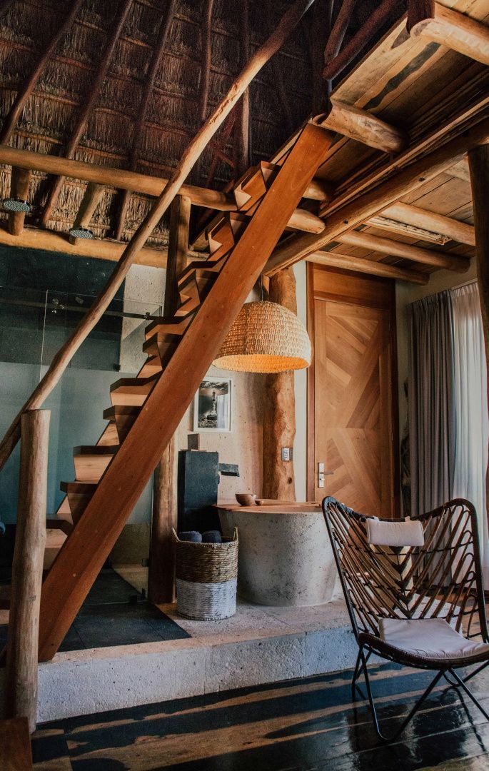 Holztreppe und freistehende Steinbadewanne unter einer mit Stroh gedeckten Decke.