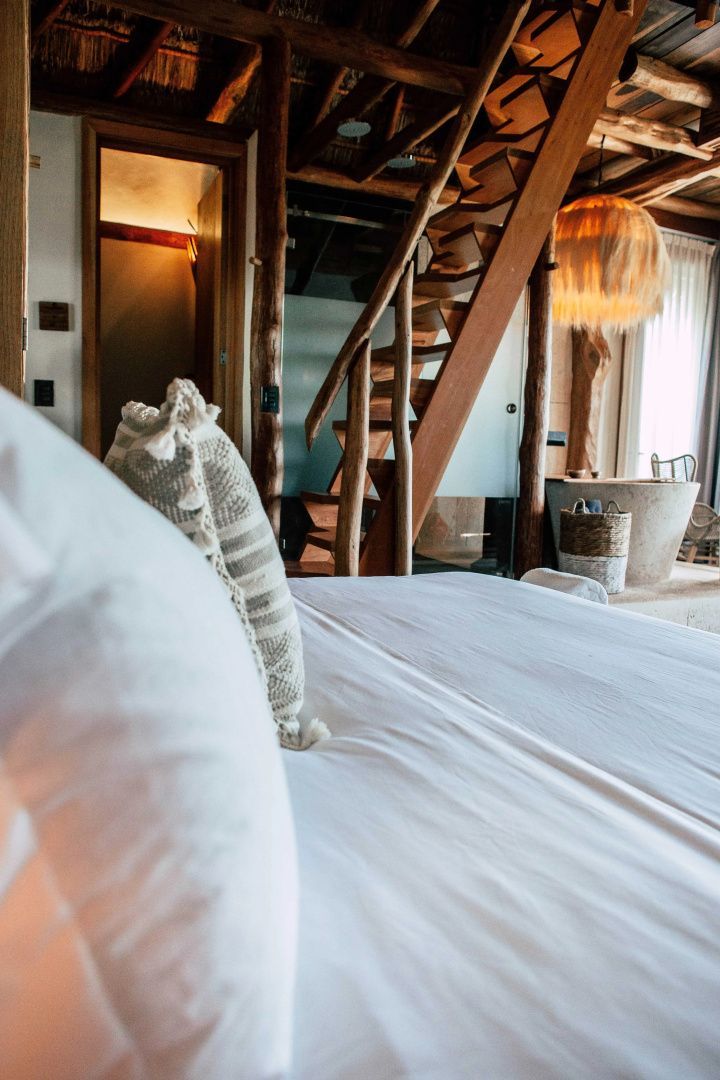Schlafbereich mit weißem Bett, Holztreppe im Hintergrund und Blick auf die Badewanne.