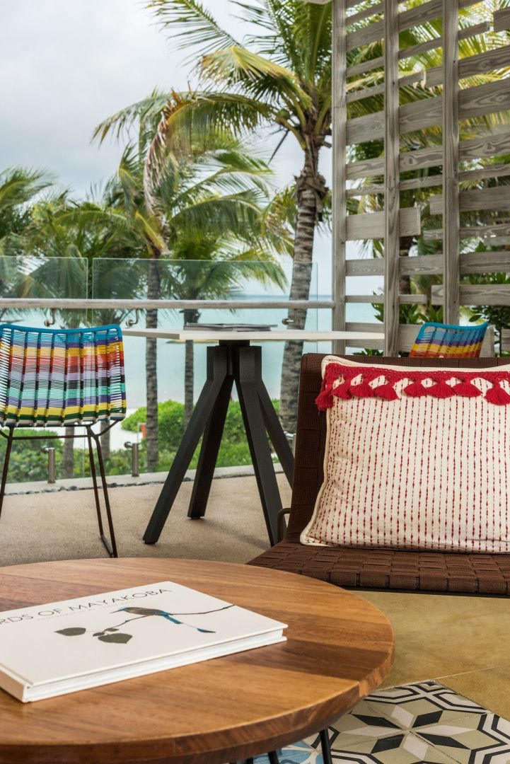 Nahaufnahme einer Terrasse mit einem Tisch, verziertem Kissen und Blick auf Palmen.