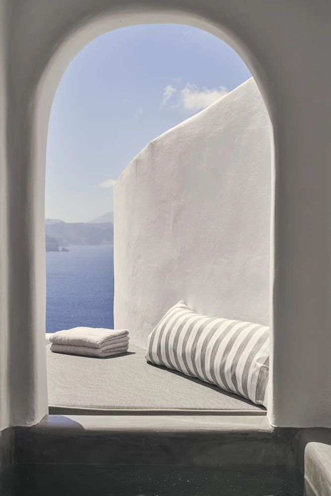 Tagesbett mit gestreiftem Kissen auf einer weißen Terrasse mit Blick auf das blaue Meer.
