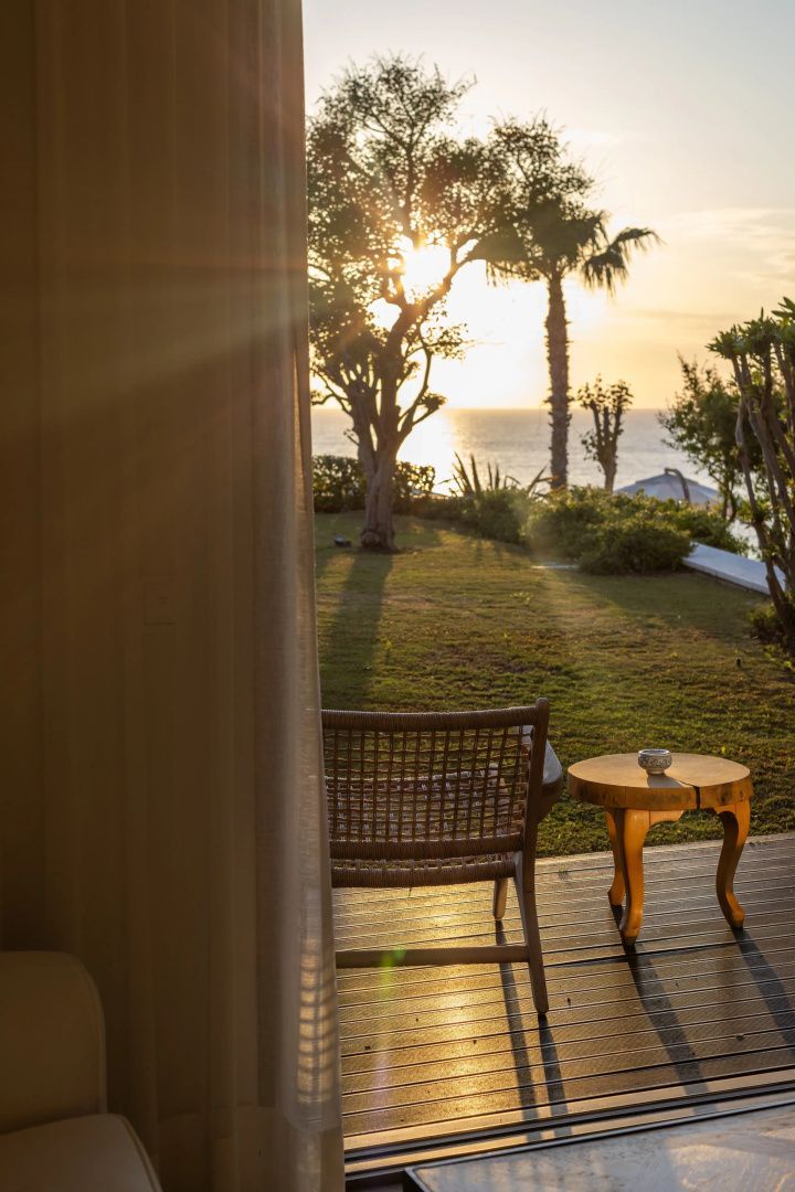 Blick von einer Holzterrasse auf den Garten und das Meer bei Sonnenuntergang.
