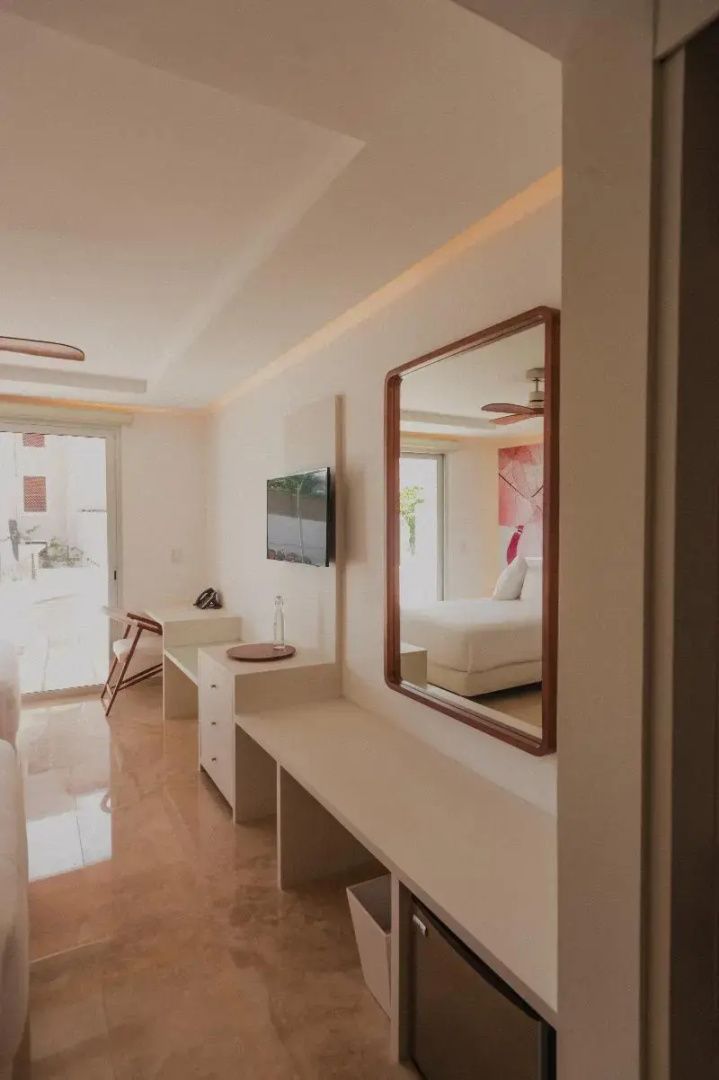 Moderner Wohnbereich eines Hotelzimmers mit Schreibtisch, Wandspiegel und Fernseher.