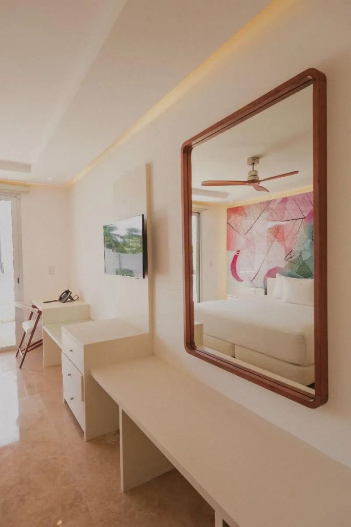 Helles Hotelzimmer mit großem Wandspiegel, Flachbild-TV und Doppelbett mit Wandmotiv.