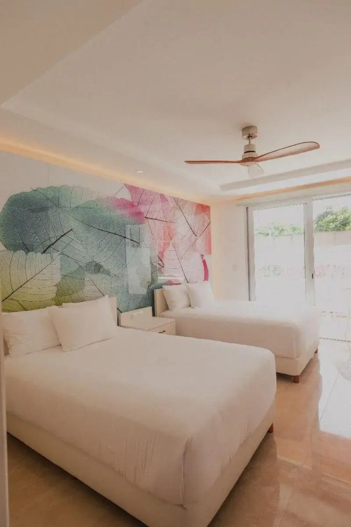 Hotelzimmer mit zwei großen Doppelbetten, Deckenventilator und bunt gestaltetem Wandbild.