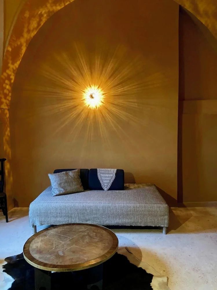 Sitzbereich mit Tagesbett und leuchtender Wandlampe an einer terracottafarbenen Wand.