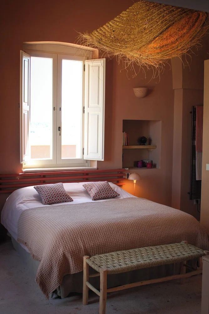 Doppelbett in einem hellen Zimmer mit terrakottafarbenen Wänden und Fenster mit Läden.