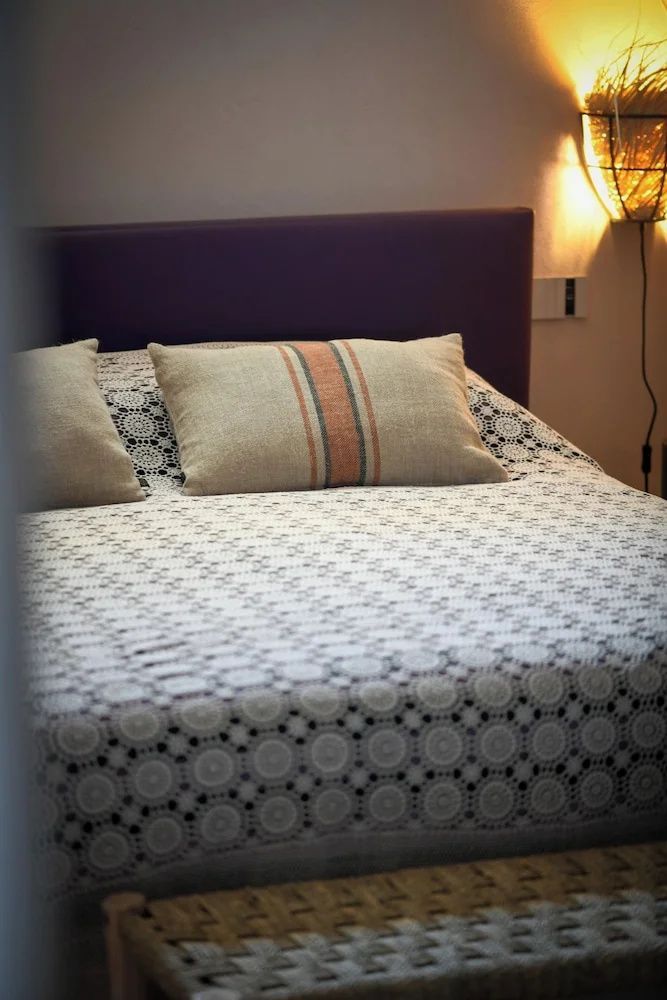 Doppelbett mit gemusterter Tagesdecke, beigen Kissen und dunklem Kopfteil.